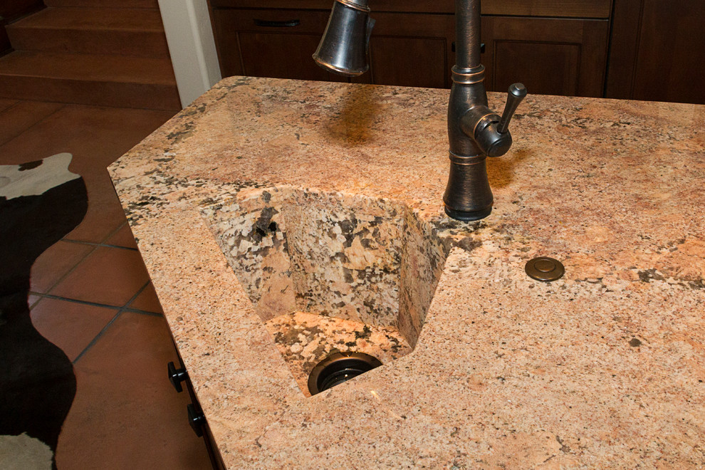 This is an example of a galley enclosed kitchen in Phoenix with a submerged sink, flat-panel cabinets, dark wood cabinets, granite worktops, white splashback, stone tiled splashback, integrated appliances, concrete flooring and an island.