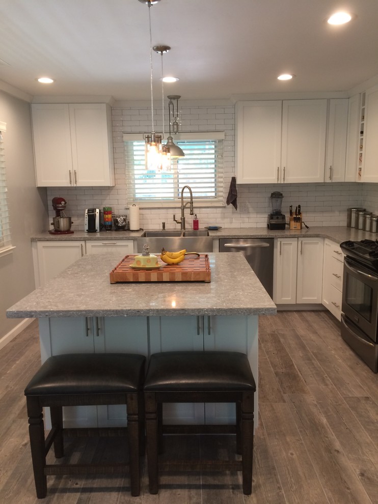 Inspiration for a medium sized classic l-shaped kitchen/diner in San Luis Obispo with a belfast sink, shaker cabinets, white cabinets, engineered stone countertops, grey splashback, metro tiled splashback, stainless steel appliances, porcelain flooring, an island and grey floors.