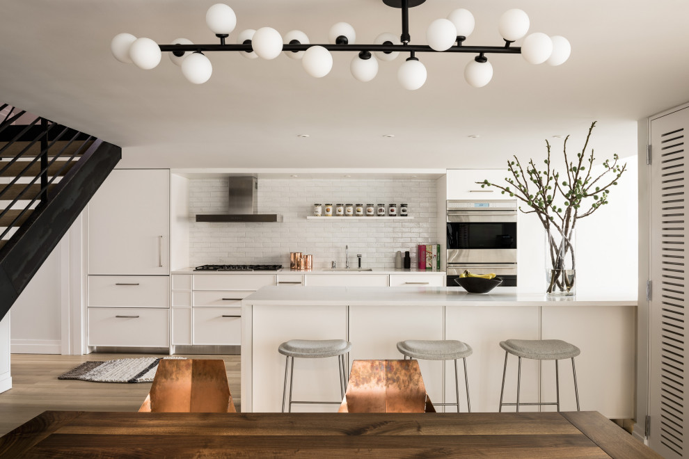 Inspiration for a large contemporary galley light wood floor and beige floor eat-in kitchen remodel in New York with white cabinets, white backsplash, ceramic backsplash, stainless steel appliances, an island, flat-panel cabinets and white countertops