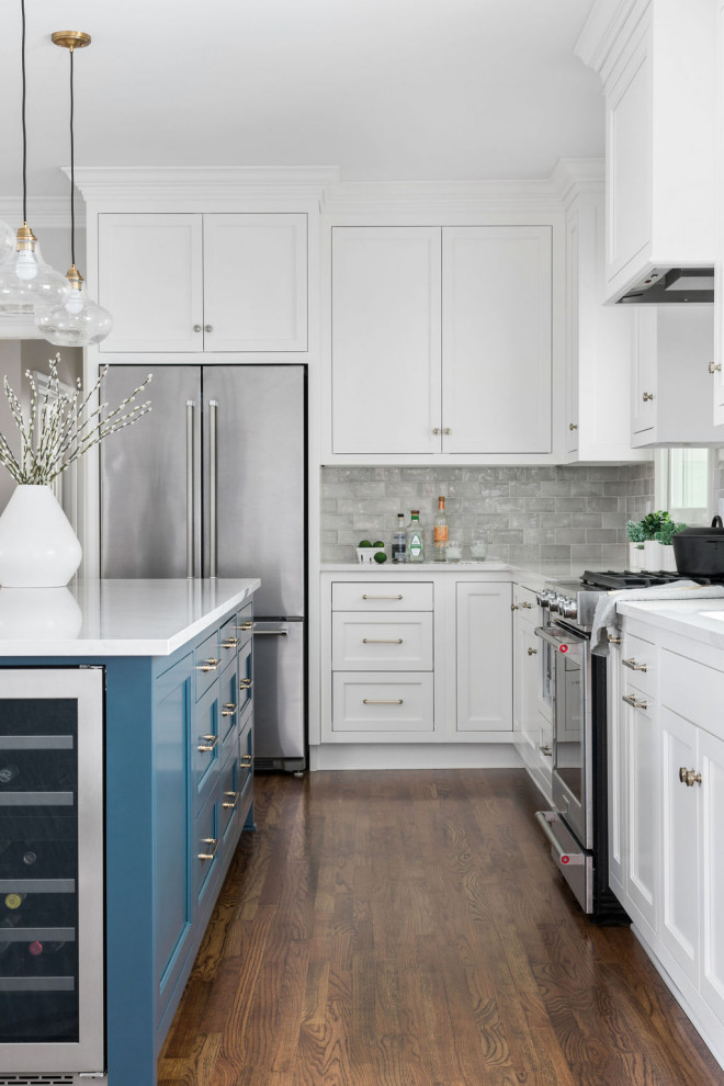 This is an example of a medium sized traditional l-shaped kitchen in Atlanta with a submerged sink, recessed-panel cabinets, white cabinets, engineered stone countertops, grey splashback, porcelain splashback, stainless steel appliances, medium hardwood flooring, an island, brown floors and white worktops.