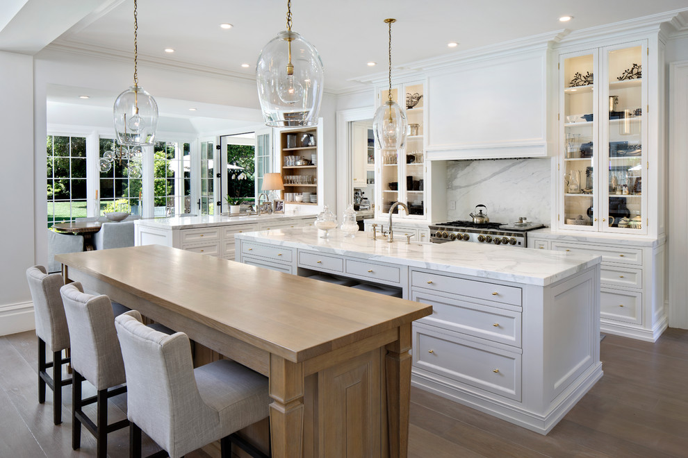 Elegant light wood floor and beige floor eat-in kitchen photo in San Francisco with glass-front cabinets, white cabinets, white backsplash, stone slab backsplash, stainless steel appliances, two islands and white countertops