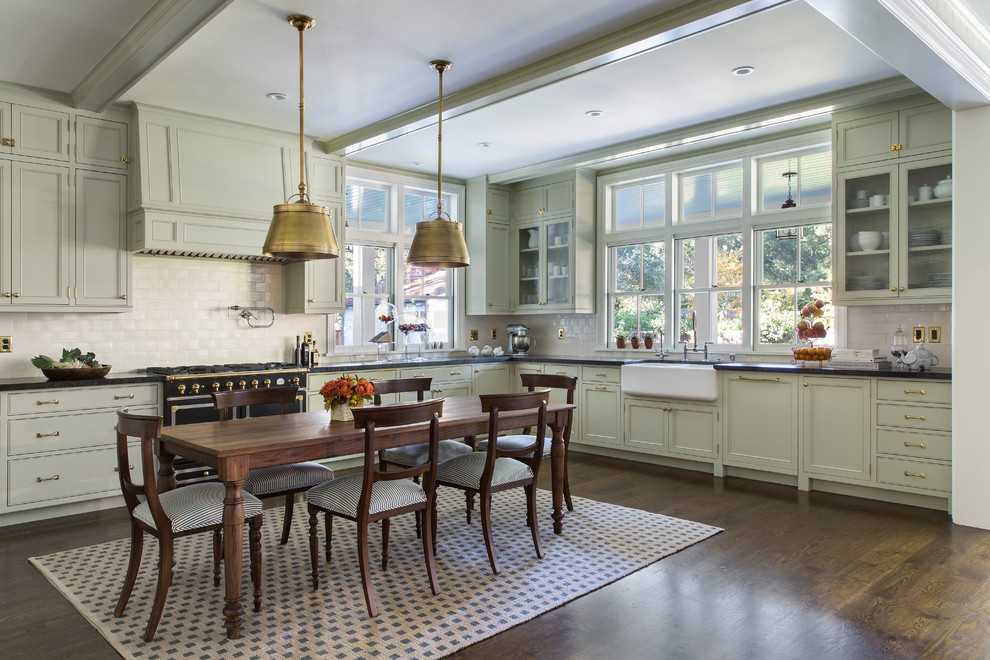 Inspiration for a mid-sized transitional l-shaped dark wood floor and brown floor eat-in kitchen remodel in San Francisco with a farmhouse sink, recessed-panel cabinets, green cabinets, white backsplash, black appliances, solid surface countertops, porcelain backsplash and an island