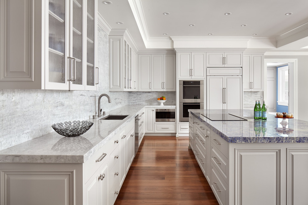 Bild på ett vintage grå grått l-kök, med en undermonterad diskho, luckor med upphöjd panel, vita skåp, grått stänkskydd, rostfria vitvaror, mellanmörkt trägolv, en köksö och brunt golv