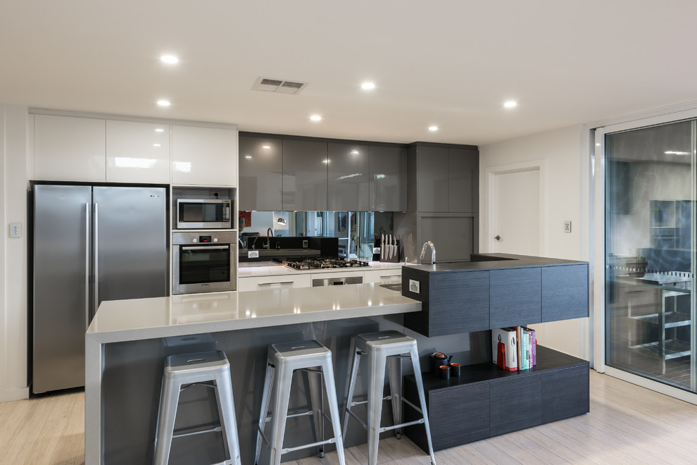 Mid-sized trendy galley bamboo floor kitchen pantry photo in Adelaide with an undermount sink, flat-panel cabinets, dark wood cabinets, quartz countertops, metallic backsplash, mirror backsplash, stainless steel appliances and an island