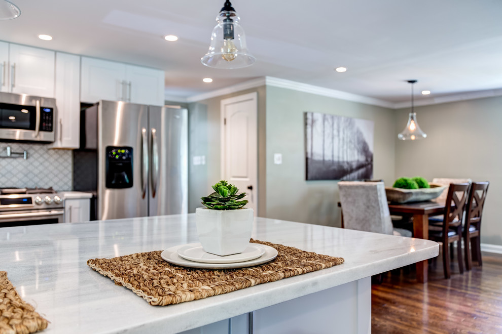 Photo of a medium sized classic u-shaped kitchen in Atlanta with a built-in sink, white cabinets, white splashback, stainless steel appliances, medium hardwood flooring, a breakfast bar, brown floors and white worktops.