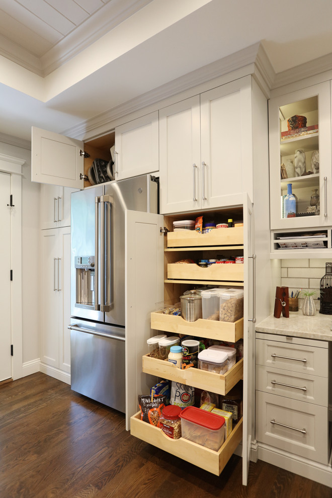 Bild på ett mellanstort vintage beige beige kök, med en undermonterad diskho, luckor med infälld panel, vita skåp, bänkskiva i kvartsit, vitt stänkskydd, stänkskydd i porslinskakel, rostfria vitvaror, mellanmörkt trägolv, en köksö och brunt golv
