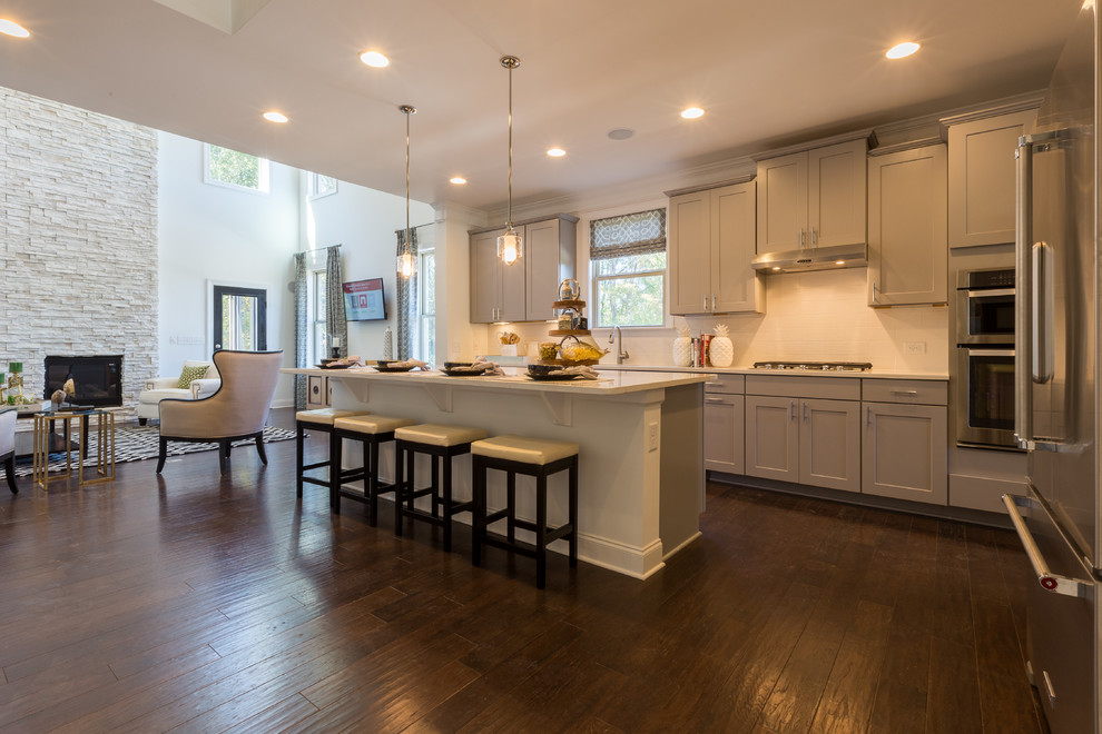 Offene Moderne Küche mit grauen Schränken, Küchenrückwand in Weiß, Küchengeräten aus Edelstahl, braunem Holzboden und Kücheninsel in Atlanta