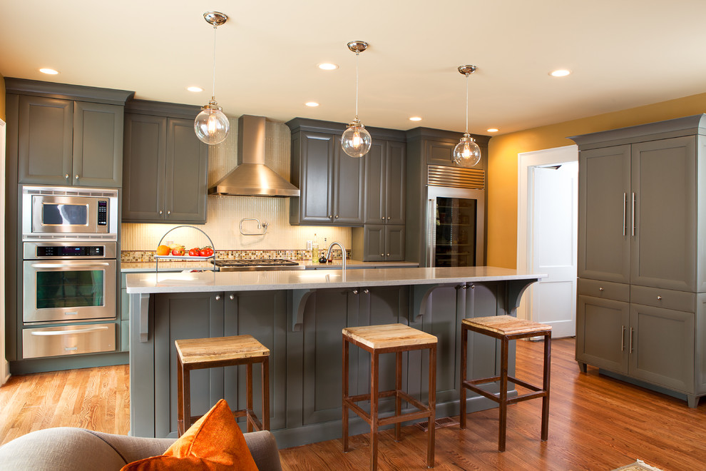 Inredning av ett klassiskt mellanstort kök, med en undermonterad diskho, luckor med infälld panel, grå skåp, granitbänkskiva, vitt stänkskydd, stänkskydd i glaskakel, rostfria vitvaror, mellanmörkt trägolv, en köksö och brunt golv