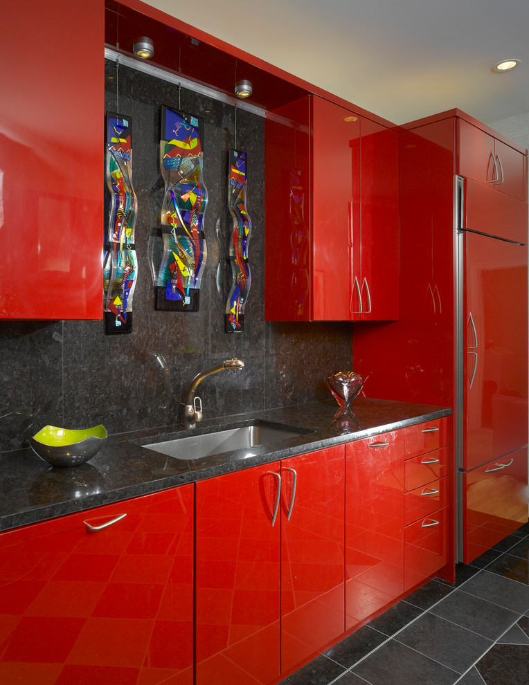 Aménagement d'une cuisine parallèle moderne avec un évier 1 bac, des portes de placard rouges, une crédence noire et un électroménager en acier inoxydable.