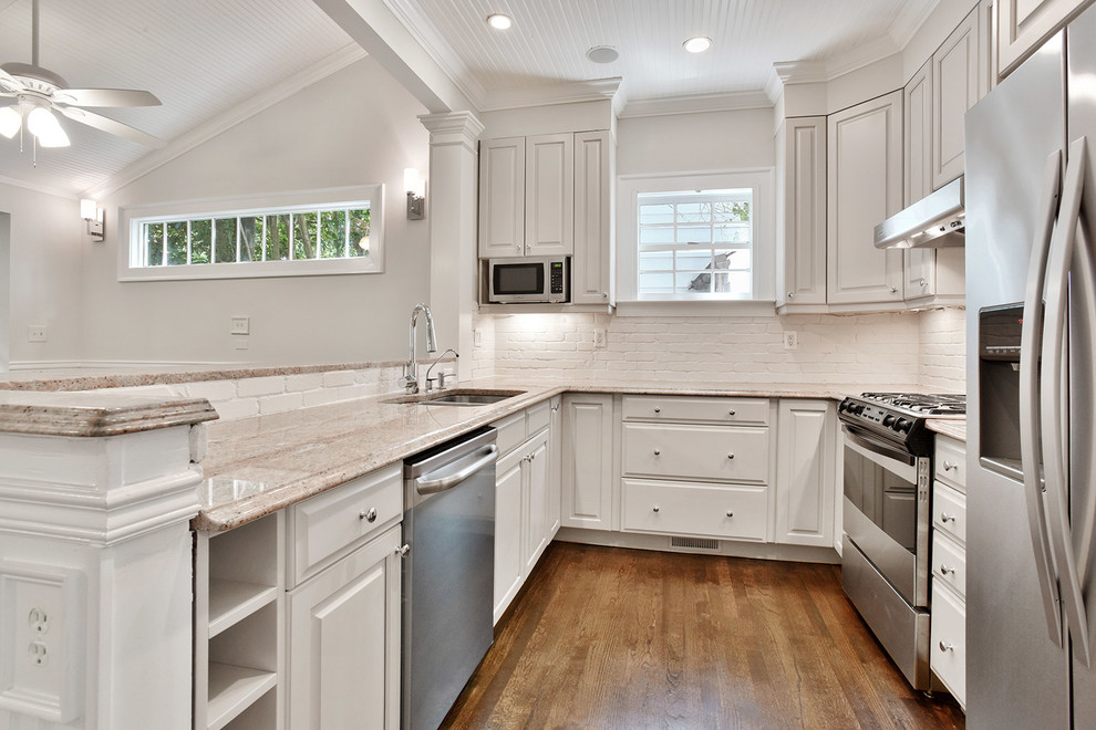 Bild på ett litet 50 tals flerfärgad flerfärgat kök, med en undermonterad diskho, luckor med upphöjd panel, grå skåp, granitbänkskiva, grått stänkskydd, stänkskydd i tegel, rostfria vitvaror, mörkt trägolv, en halv köksö och brunt golv