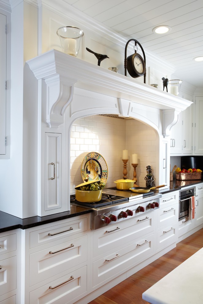 Example of a large classic l-shaped medium tone wood floor eat-in kitchen design in New York with a farmhouse sink, white cabinets, onyx countertops, white backsplash, paneled appliances, an island, recessed-panel cabinets and subway tile backsplash