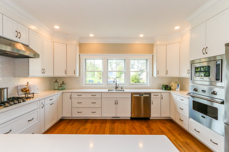 Bild på ett stort vintage kök, med en nedsänkt diskho, luckor med infälld panel, vita skåp, marmorbänkskiva, vitt stänkskydd, stänkskydd i stenkakel, rostfria vitvaror, mellanmörkt trägolv och en halv köksö