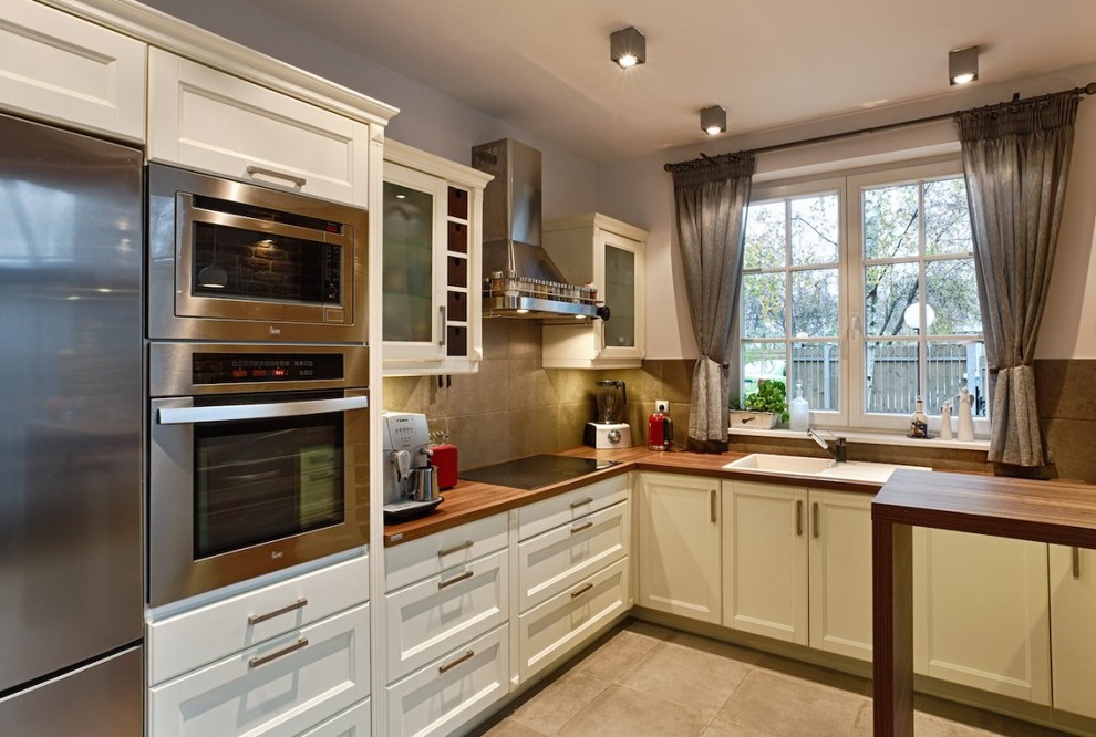 Expansive contemporary l-shaped kitchen/diner in Glasgow with an integrated sink, shaker cabinets, beige cabinets, wood worktops, grey splashback, ceramic splashback, stainless steel appliances, ceramic flooring and a breakfast bar.