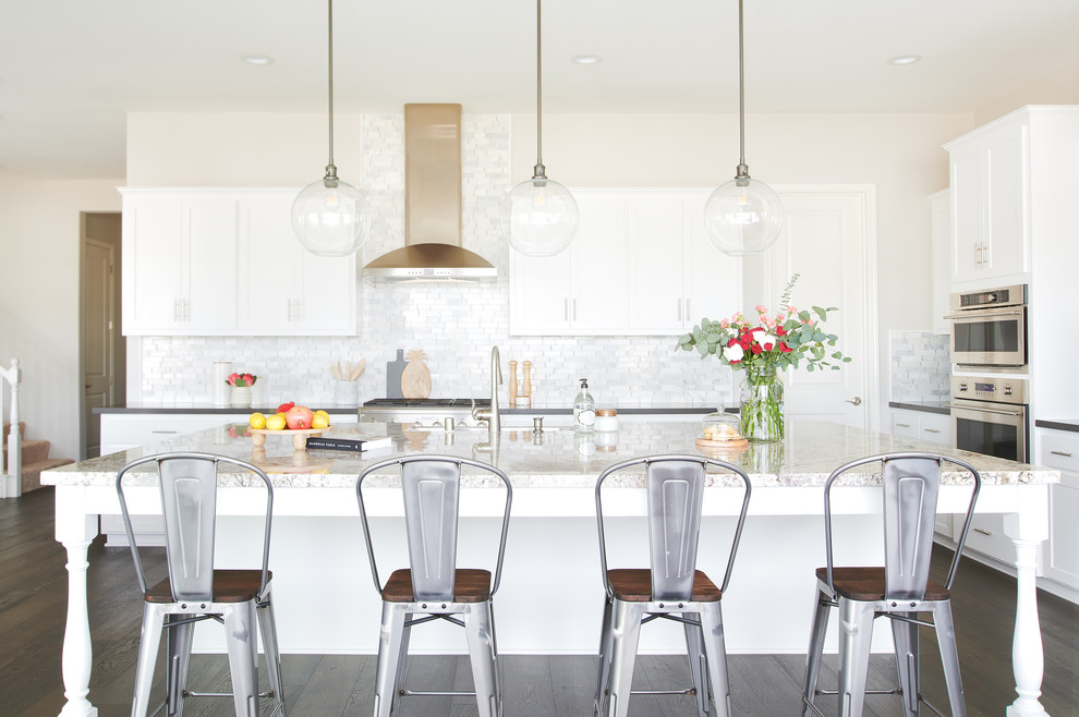 Inredning av ett klassiskt kök, med en undermonterad diskho, skåp i shakerstil, vita skåp, vitt stänkskydd, stänkskydd i marmor, rostfria vitvaror och en köksö