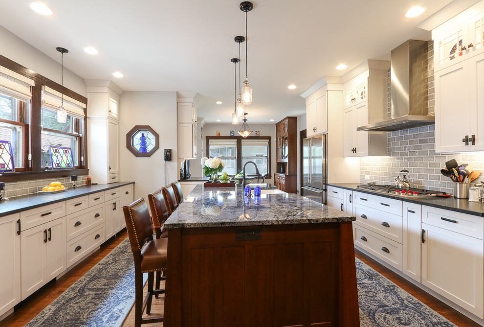 Inspiration for a large craftsman medium tone wood floor enclosed kitchen remodel in Chicago with a farmhouse sink, shaker cabinets, white cabinets, granite countertops, gray backsplash, ceramic backsplash, stainless steel appliances and an island