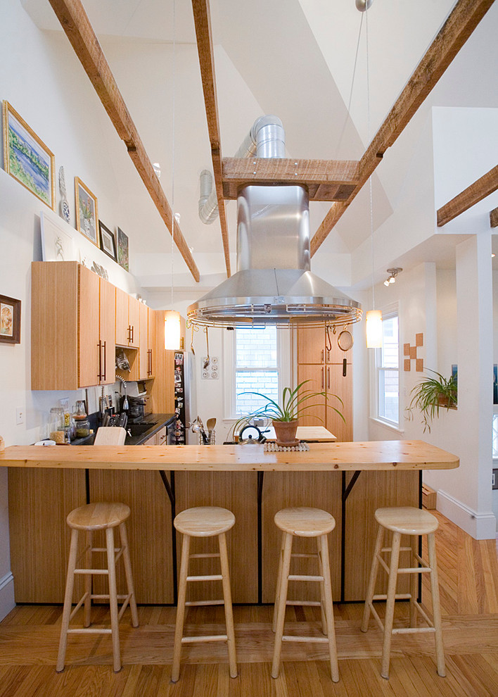 Large country u-shaped kitchen/diner in Boston with flat-panel cabinets, medium wood cabinets, wood worktops, a submerged sink, stainless steel appliances, light hardwood flooring and an island.