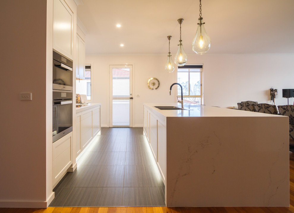 Inspiration for a large classic galley kitchen/diner in Melbourne with a built-in sink, shaker cabinets, white cabinets, engineered stone countertops, stone slab splashback, black appliances and an island.