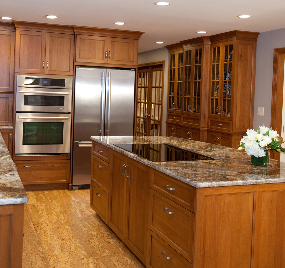Klassisk inredning av ett mellanstort kök, med en undermonterad diskho, luckor med infälld panel, skåp i mellenmörkt trä, granitbänkskiva, grått stänkskydd, stänkskydd i keramik, rostfria vitvaror, betonggolv, en köksö och brunt golv