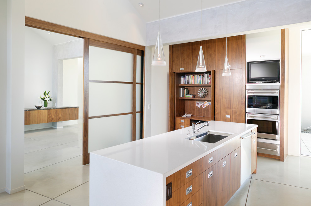 Inredning av ett modernt l-kök, med en undermonterad diskho, släta luckor, skåp i mellenmörkt trä, marmorbänkskiva, vitt stänkskydd, rostfria vitvaror, marmorgolv och en köksö