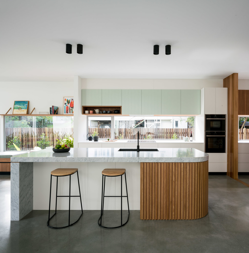 Retro galley open plan kitchen in Brisbane with a single-bowl sink, flat-panel cabinets, white cabinets, window splashback, concrete flooring, an island, grey floors and grey worktops.