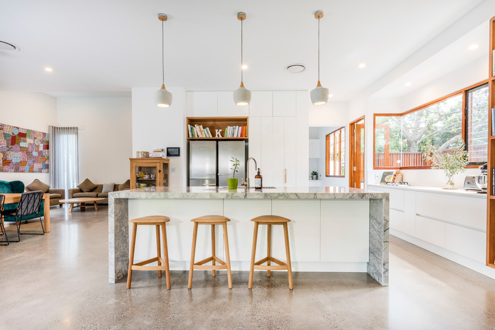 Foto på ett funkis grå kök med öppen planlösning, med en undermonterad diskho, släta luckor, vita skåp, vitt stänkskydd, rostfria vitvaror, betonggolv, en köksö och grått golv