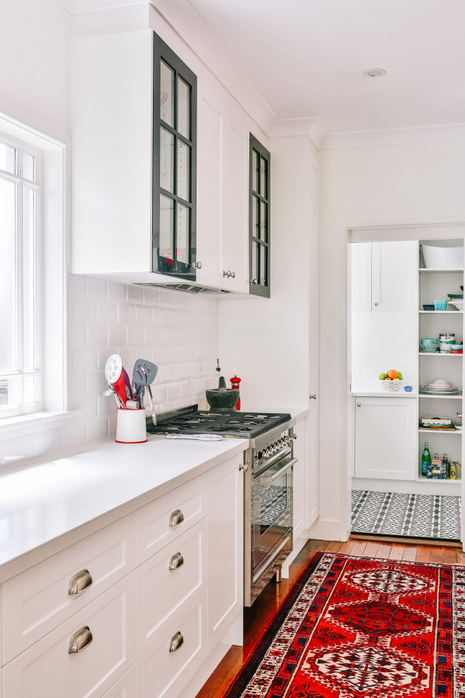 Klassische Küche mit Schrankfronten im Shaker-Stil, weißen Schränken, Küchenrückwand in Weiß, Rückwand aus Metrofliesen, braunem Holzboden und Kücheninsel in Brisbane