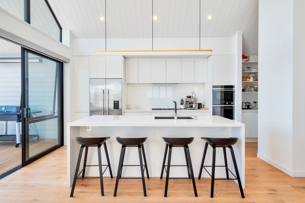 Inspiration for a contemporary galley open plan kitchen in Other with a submerged sink, flat-panel cabinets, white cabinets, white splashback, stainless steel appliances, medium hardwood flooring, an island, brown floors, white worktops, a timber clad ceiling and a vaulted ceiling.