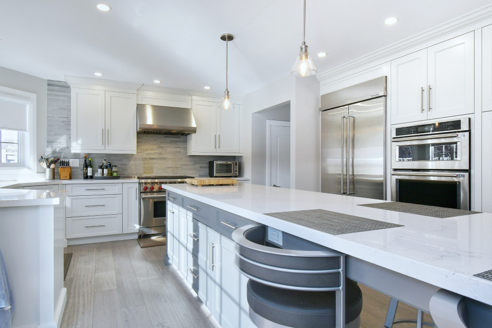 Photo of a large traditional l-shaped kitchen/diner in Toronto with a submerged sink, recessed-panel cabinets, white cabinets, engineered stone countertops, grey splashback, mosaic tiled splashback, stainless steel appliances, medium hardwood flooring, an island, brown floors and white worktops.