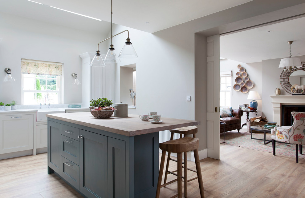 Idées déco pour une cuisine ouverte classique en L avec un évier de ferme, un placard à porte affleurante, des portes de placards vertess, un plan de travail en quartz, une crédence verte, une crédence en carreau de porcelaine, un électroménager noir, parquet clair, îlot et un plan de travail blanc.
