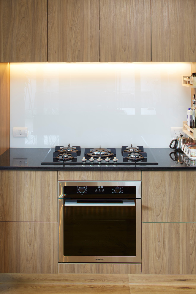 Expansive contemporary u-shaped kitchen/diner in Christchurch with a built-in sink, glass-front cabinets, white cabinets, granite worktops, white splashback, glass sheet splashback, black appliances, plywood flooring and a breakfast bar.