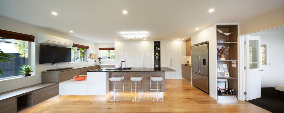 Design ideas for an expansive contemporary u-shaped kitchen/diner in Christchurch with a built-in sink, glass-front cabinets, white cabinets, granite worktops, white splashback, glass sheet splashback, black appliances, plywood flooring and a breakfast bar.
