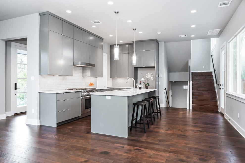 Contemporary galley kitchen/diner in Austin with a single-bowl sink, flat-panel cabinets, grey cabinets, engineered stone countertops, white splashback, metro tiled splashback, stainless steel appliances, medium hardwood flooring and an island.