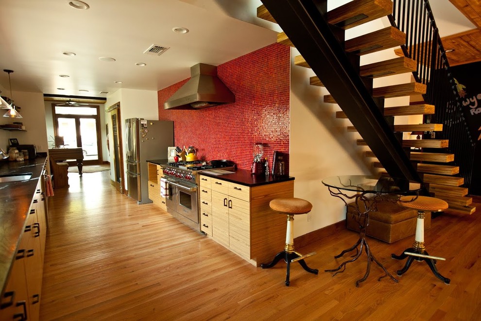 デンバーにある小さなモダンスタイルのおしゃれなキッチン (ドロップインシンク、フラットパネル扉のキャビネット、中間色木目調キャビネット、赤いキッチンパネル、シルバーの調理設備、淡色無垢フローリング) の写真