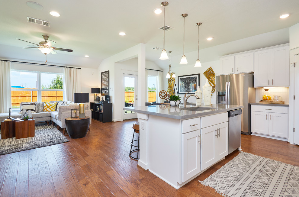 Mid-sized trendy l-shaped medium tone wood floor and brown floor eat-in kitchen photo in Austin with an undermount sink, recessed-panel cabinets, white cabinets, solid surface countertops, white backsplash, ceramic backsplash, stainless steel appliances, an island and gray countertops