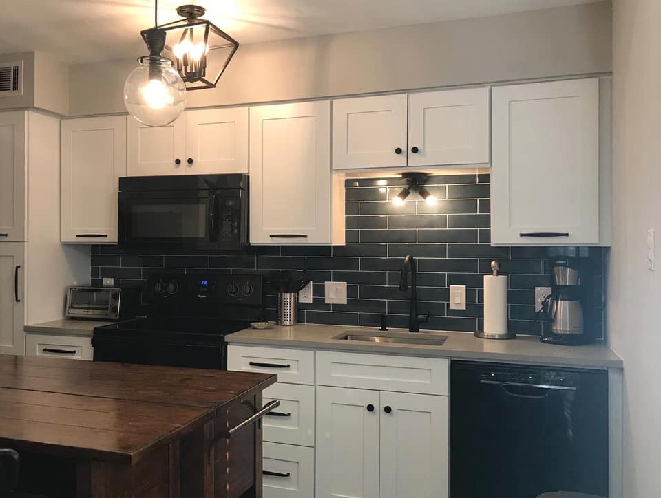 Bild på ett litet industriellt grå linjärt grått kök och matrum, med en undermonterad diskho, luckor med infälld panel, vita skåp, bänkskiva i kvarts, blått stänkskydd, stänkskydd i keramik, svarta vitvaror och en köksö