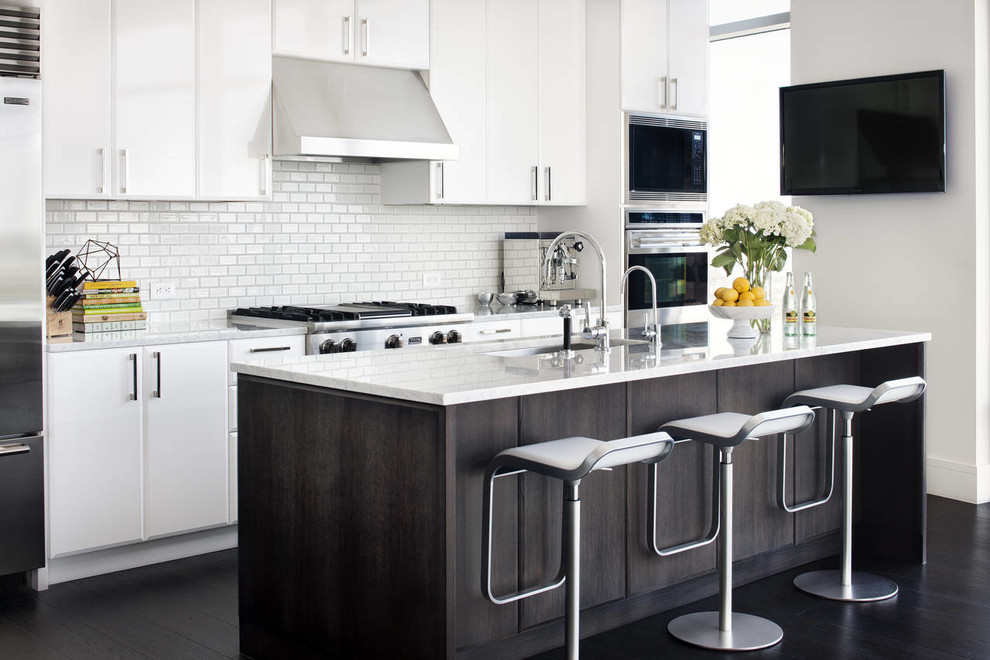 Modern inredning av ett mellanstort kök, med en undermonterad diskho, släta luckor, vita skåp, marmorbänkskiva, vitt stänkskydd, stänkskydd i tunnelbanekakel, rostfria vitvaror och mörkt trägolv