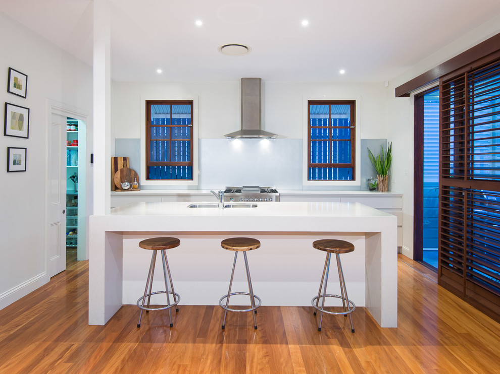 Moderne Küche mit Unterbauwaschbecken, flächenbündigen Schrankfronten, weißen Schränken, Küchengeräten aus Edelstahl, braunem Holzboden und Kücheninsel in Brisbane