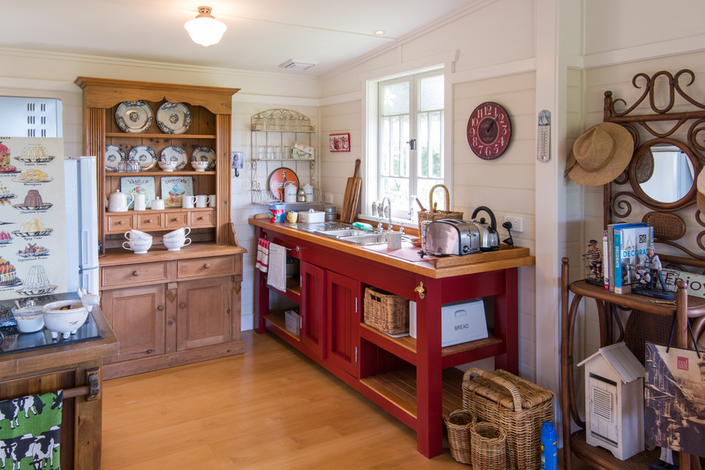 Cette image montre une cuisine rustique avec un évier posé, un placard avec porte à panneau encastré, des portes de placard rouges, un sol en bois brun et un plan de travail en bois.
