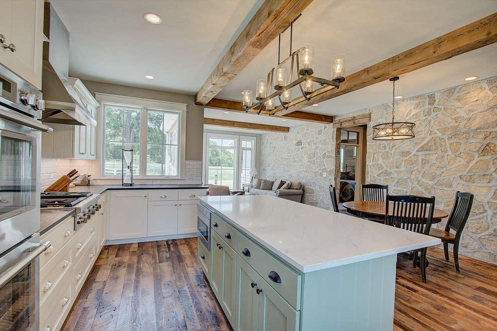 Foto på ett avskilt lantligt vit kök, med en rustik diskho, släta luckor, gröna skåp, granitbänkskiva, vitt stänkskydd, stänkskydd i tunnelbanekakel, rostfria vitvaror, ljust trägolv, en köksö och brunt golv