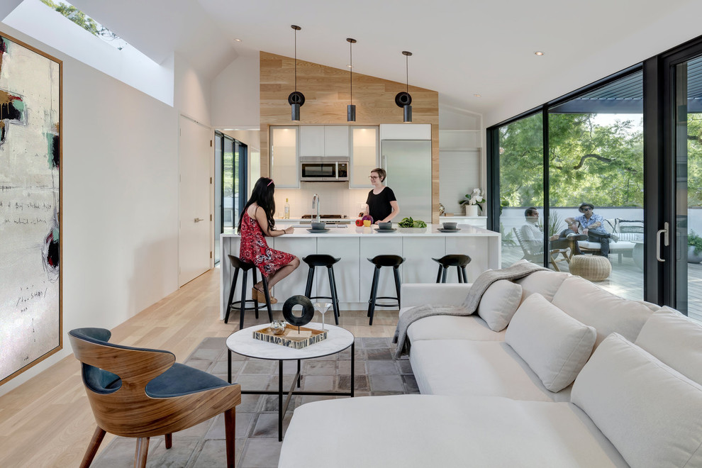 Modern open plan kitchen in Austin with glass-front cabinets, stainless steel cabinets, granite worktops, white splashback, stainless steel appliances, light hardwood flooring and an island.