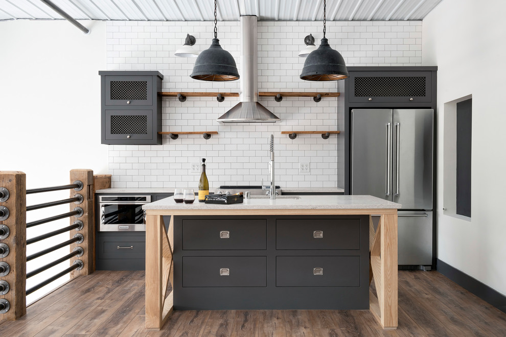 Inspiration for an urban galley kitchen in Minneapolis with white splashback, stainless steel appliances, an island, brown floors, a submerged sink, flat-panel cabinets, grey cabinets, metro tiled splashback, dark hardwood flooring and grey worktops.