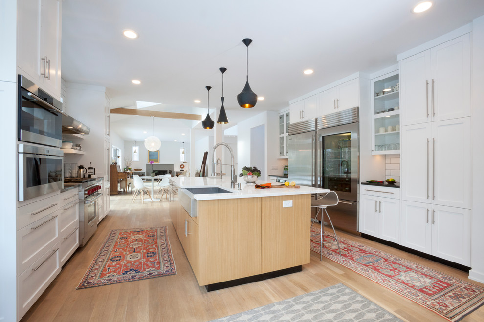 Eat-in kitchen - mid-sized contemporary galley light wood floor and brown floor eat-in kitchen idea in New York with a farmhouse sink, shaker cabinets, white cabinets, quartz countertops, white backsplash, subway tile backsplash, stainless steel appliances and an island