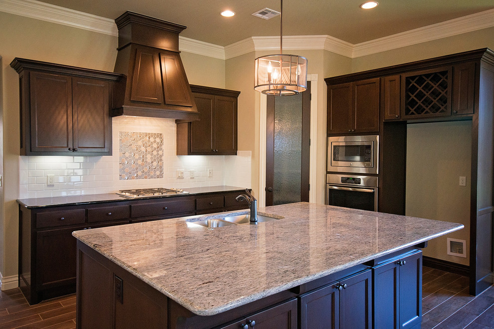 Photo of a large traditional u-shaped open plan kitchen in Oklahoma City with a submerged sink, shaker cabinets, dark wood cabinets, granite worktops, white splashback, ceramic splashback, stainless steel appliances, ceramic flooring and an island.