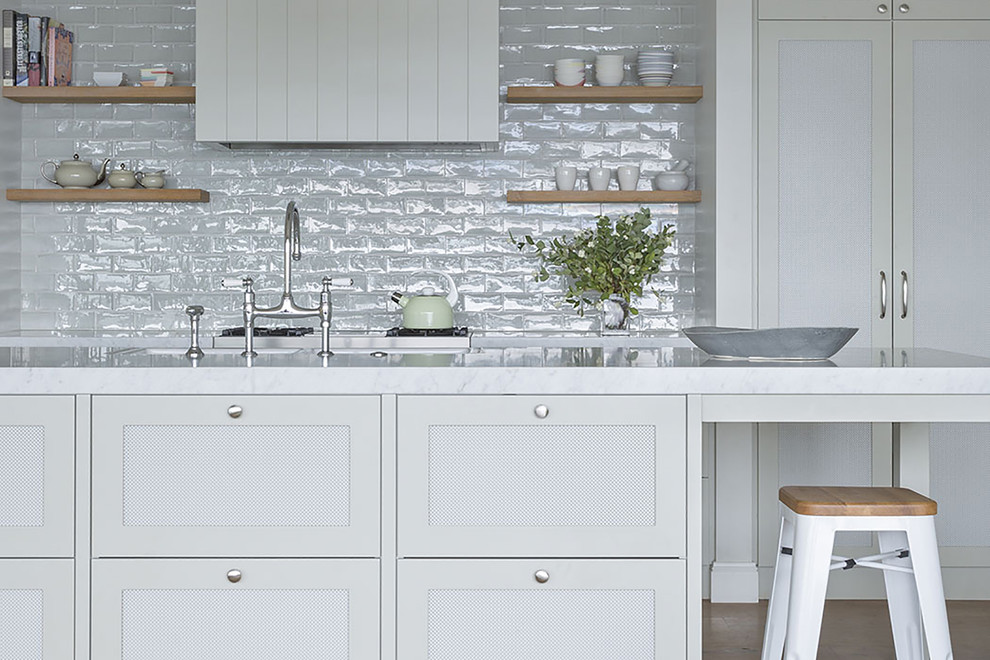 Inspiration for a large nautical galley kitchen/diner in Auckland with a belfast sink, recessed-panel cabinets, white cabinets, marble worktops, grey splashback, ceramic splashback, stainless steel appliances, light hardwood flooring, an island and beige floors.