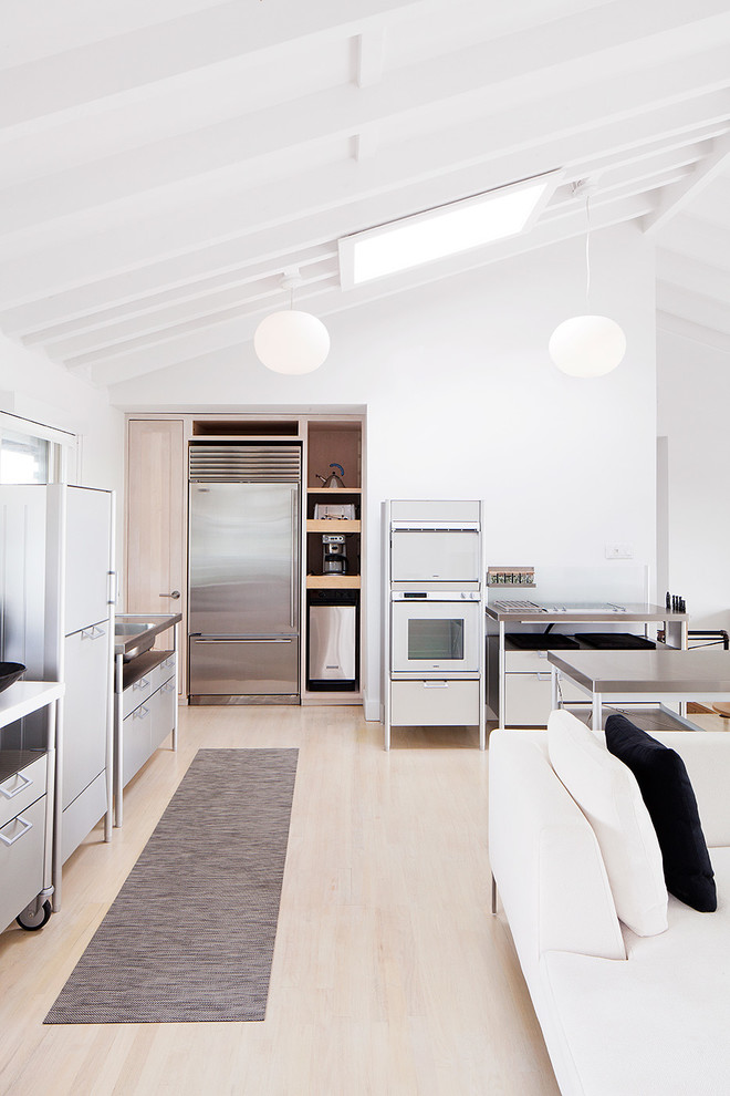Imagen de cocina escandinava abierta con electrodomésticos de acero inoxidable y suelo de madera clara