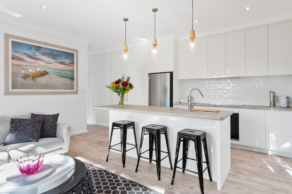 Example of a trendy galley light wood floor and beige floor open concept kitchen design in Sydney with flat-panel cabinets, white cabinets, white backsplash, stainless steel appliances, an island and gray countertops