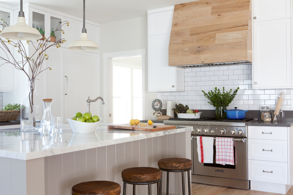 Large farmhouse l-shaped medium tone wood floor open concept kitchen photo in Los Angeles with a farmhouse sink, shaker cabinets, white cabinets, marble countertops, white backsplash, stainless steel appliances, an island and subway tile backsplash