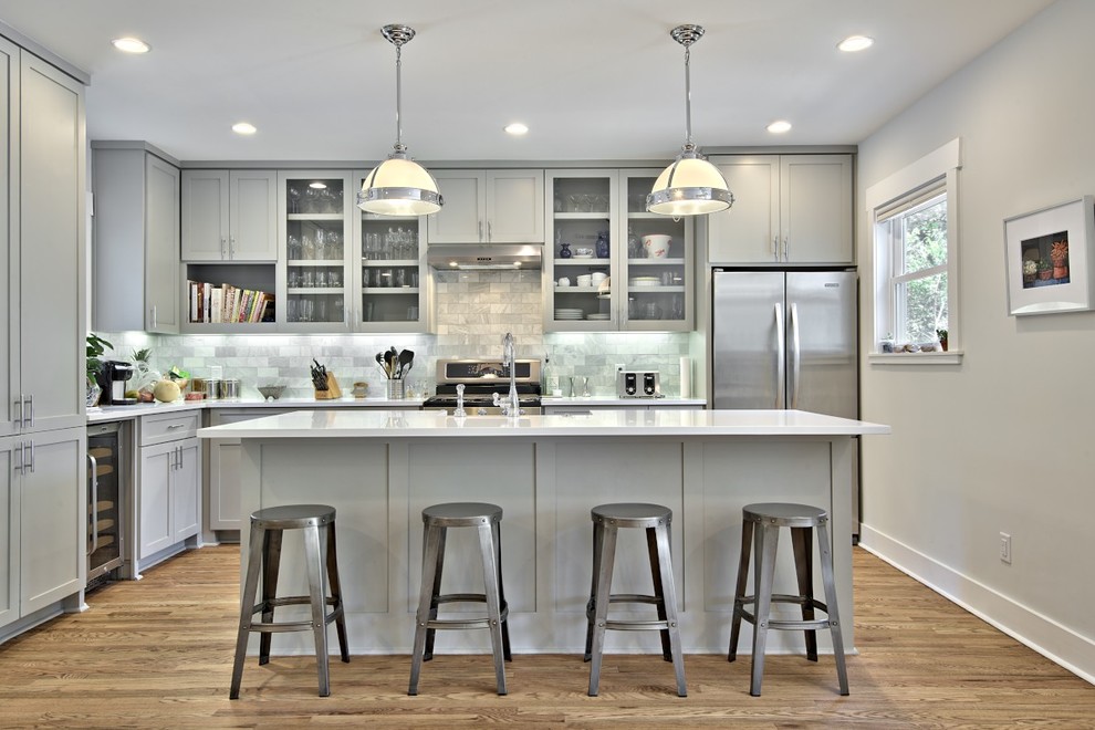 Medium tone wood floor eat-in kitchen photo in Austin with a farmhouse sink, shaker cabinets, gray cabinets, quartz countertops, gray backsplash, stone tile backsplash, stainless steel appliances and an island
