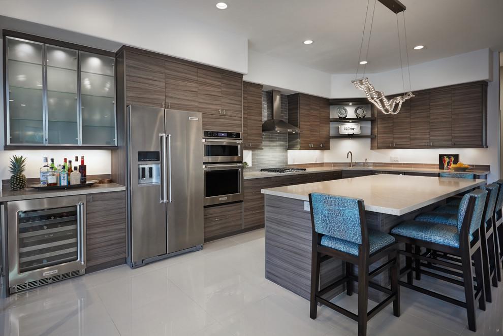 This is an example of a medium sized contemporary l-shaped kitchen/diner in Phoenix with flat-panel cabinets, grey cabinets, grey splashback, an island, a submerged sink, engineered stone countertops, glass tiled splashback, stainless steel appliances, porcelain flooring and white floors.