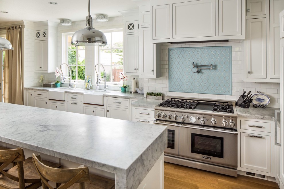 This is an example of a traditional u-shaped kitchen in Salt Lake City with a belfast sink, shaker cabinets, white cabinets, blue splashback, metro tiled splashback and stainless steel appliances.